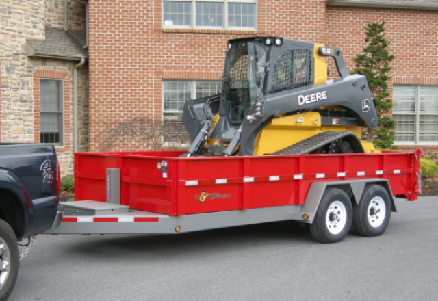red bwise dump trailer with a skid steer in it attached to a truck to pull